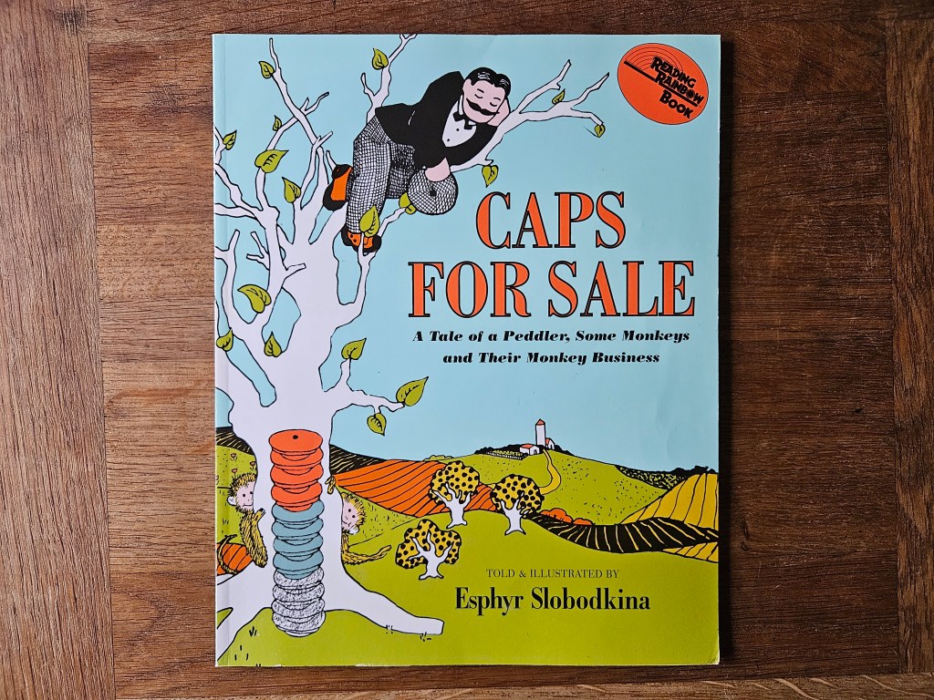 The peddler sits in a tree with monkeys; a stack of coloured caps stands beside him.